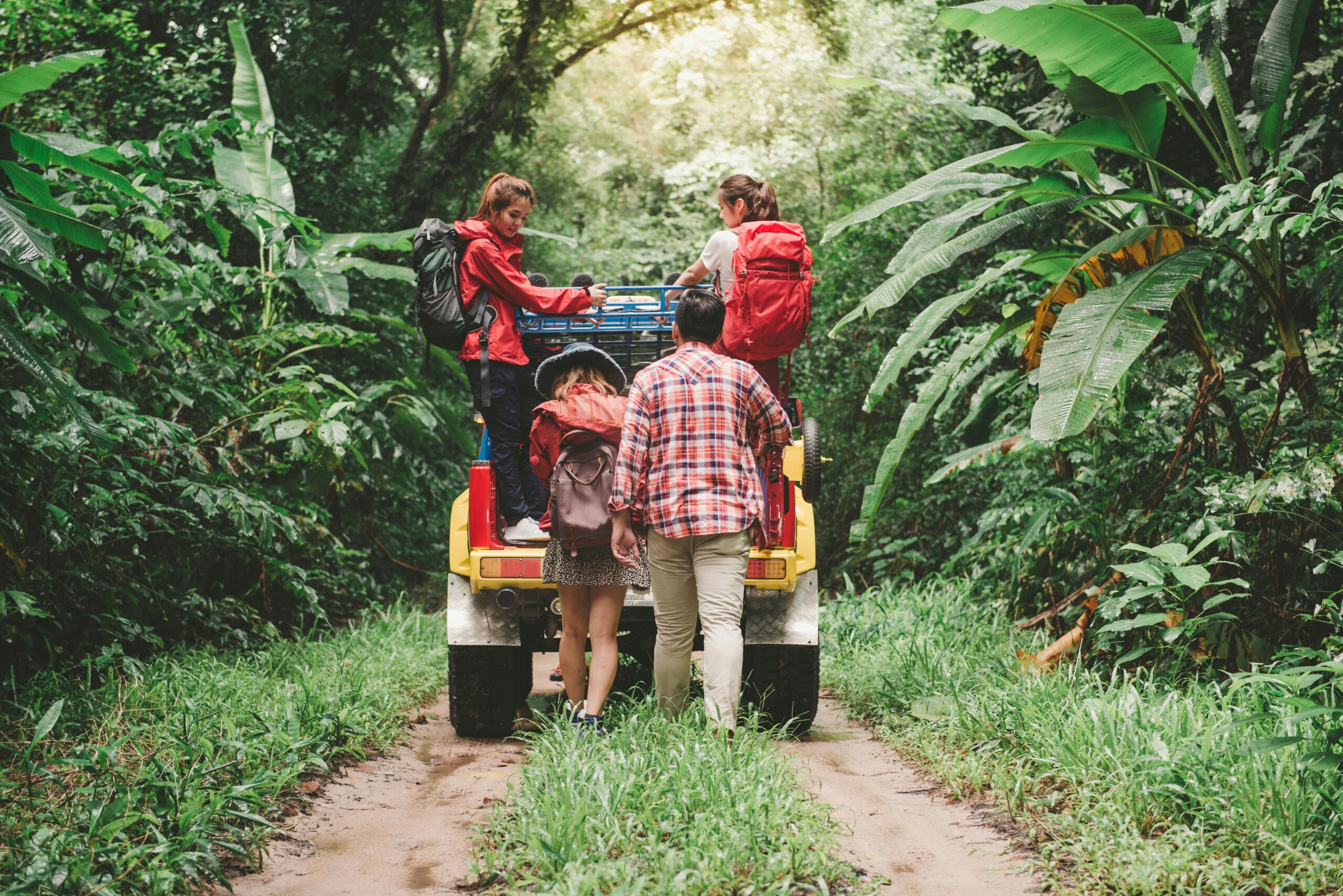Friends hiking in a tropical forest, riding a jeep with backpacks, enjoying the adventure.